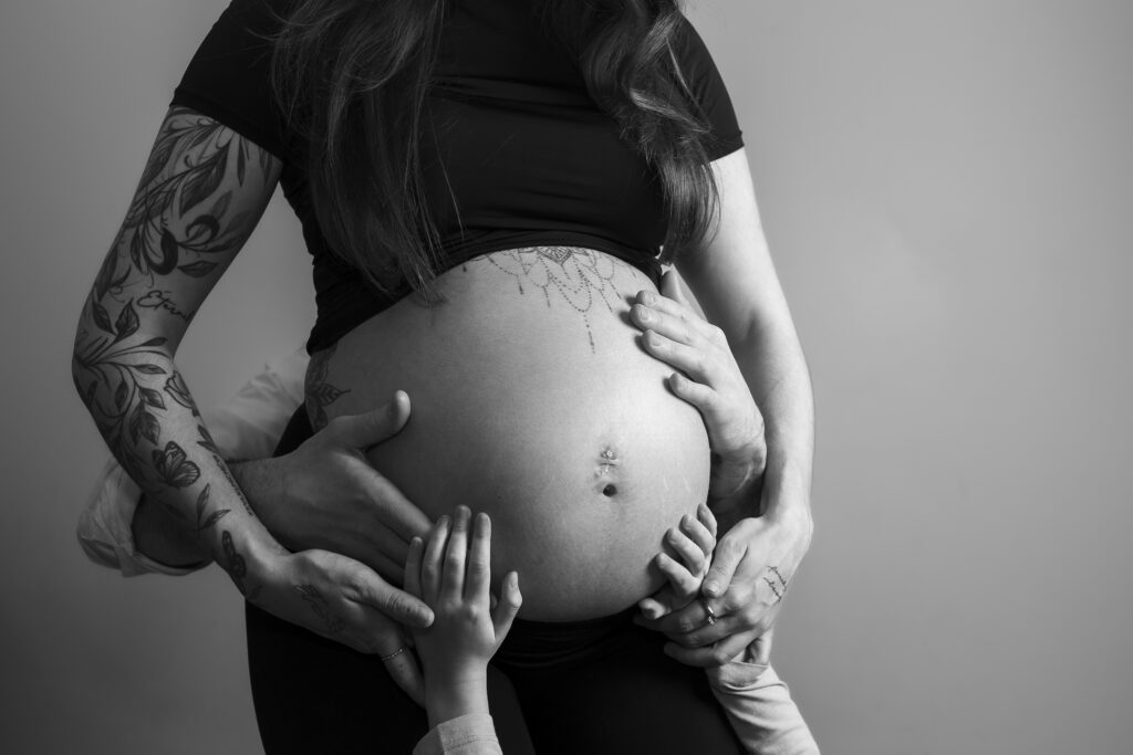Photo de grossesse d'un ventre de femme sur lequel sont posées les mains de son mari et leur fille